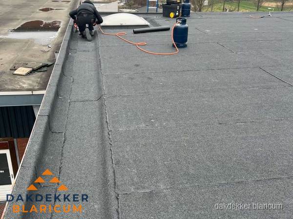 Dakdekker repareert bitumen dakbedekking op groot plat dak in Blaricum